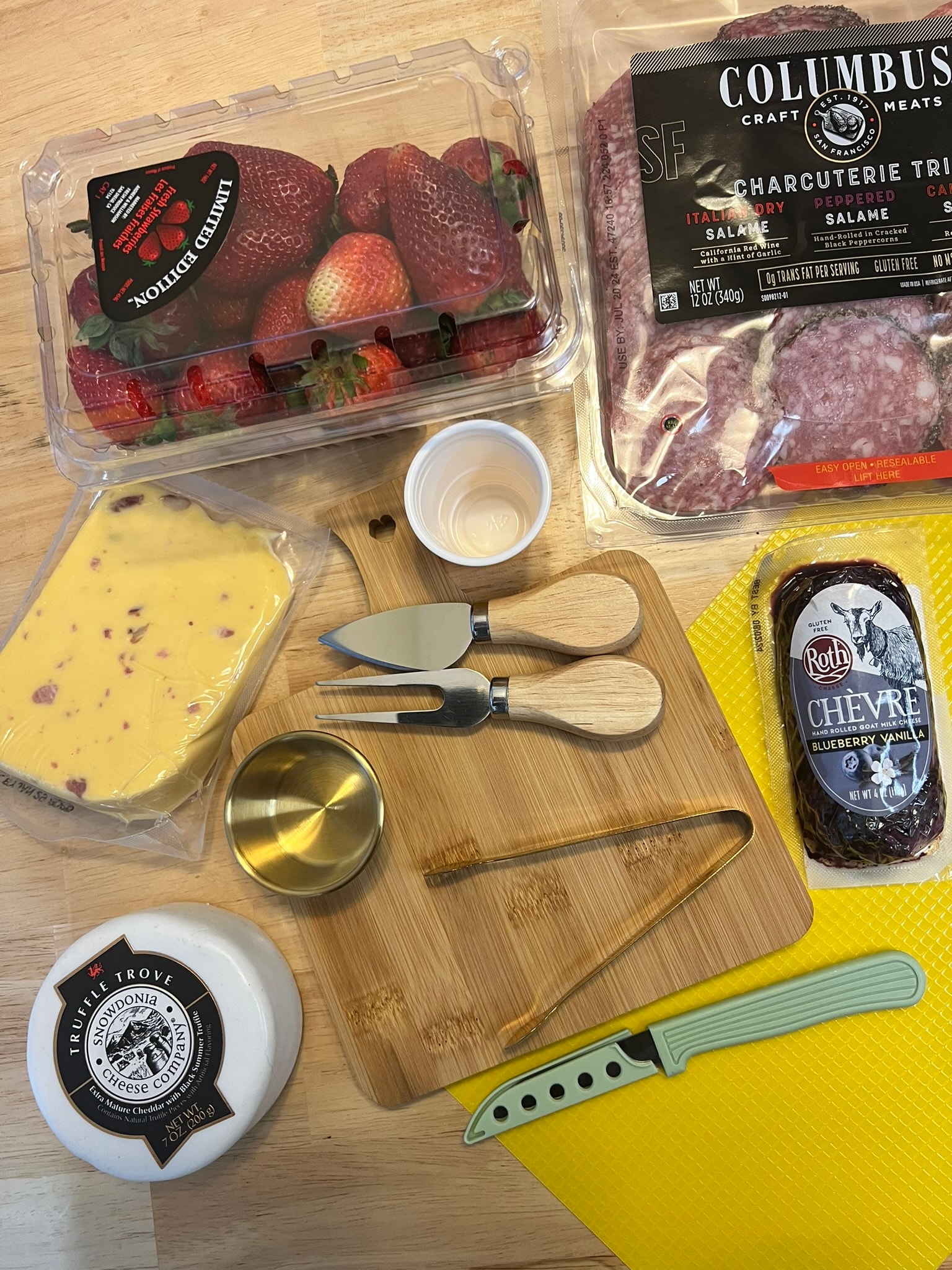 Charcuterie ingredients laid out — cheeses, meats, strawberries, tools and board